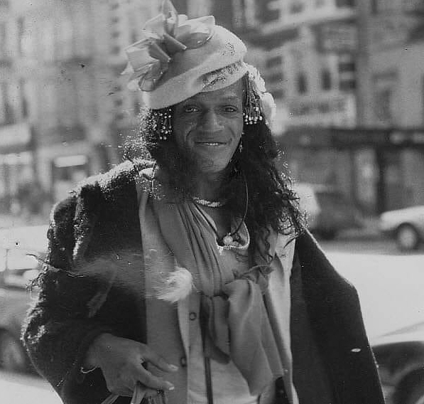 Download the full-sized image of A Photograph of Marsha P. Johnson Posing in the Street Wearing a Black Jacket with a Sweater Tied Around Her Neck